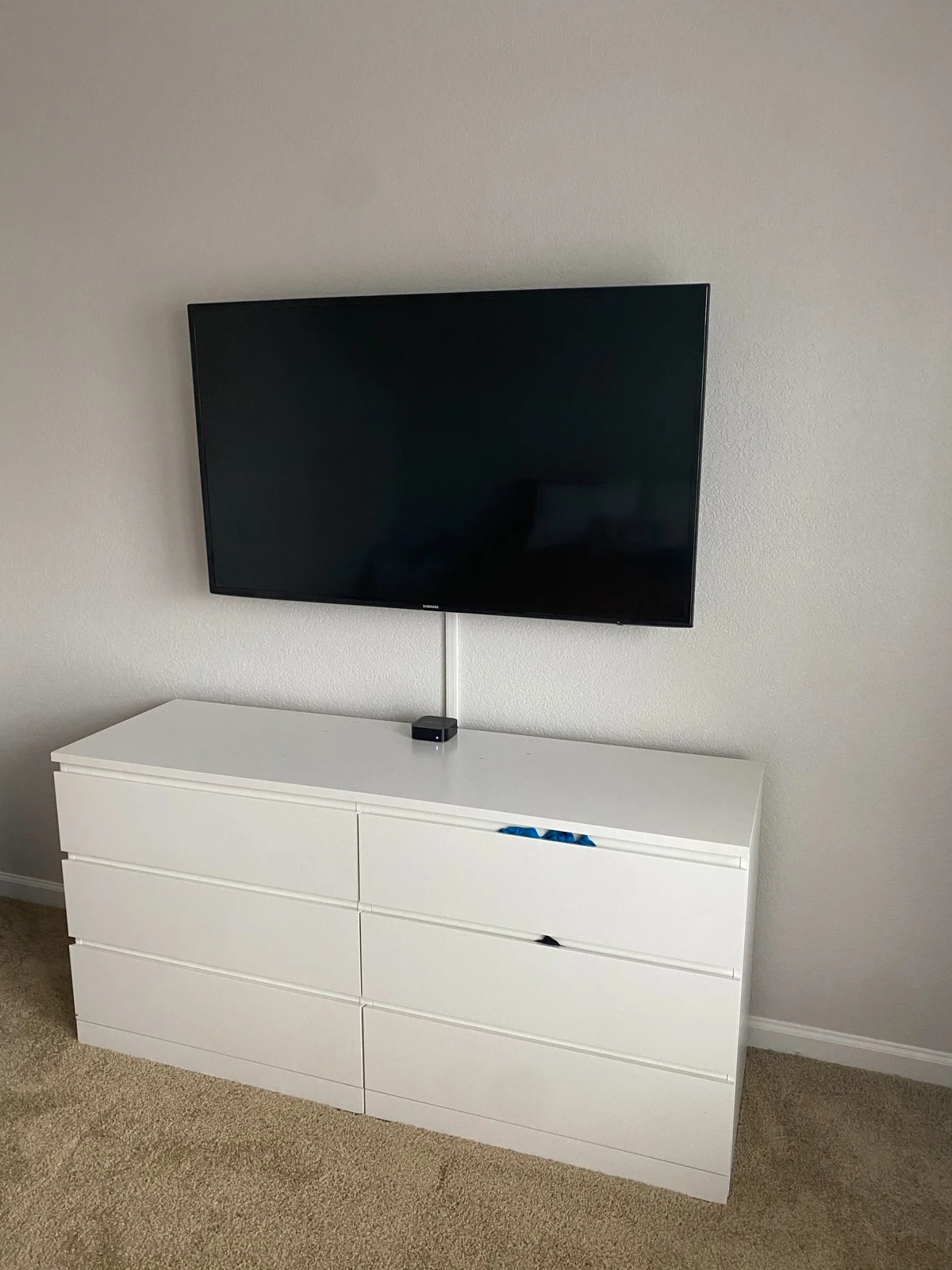 Wall-mounted television above a white dresser, with a vertical white surface cable cover leading to a small device.
